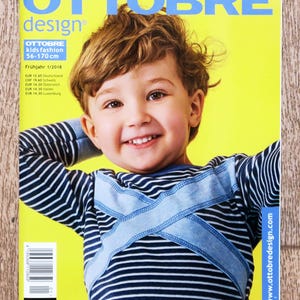 May include: A magazine cover with the title "OTTOBRE design" in blue letters on a yellow background. The cover features a smiling child wearing a blue and white striped shirt. The magazine is titled "OTTOBRE kids fashion 56-170 cm".