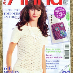 Op de afbeelding: Een tijdschriftcover met een vrouw die een wit gehaakt topje en een ketting draagt. Het tijdschrift heet "Anna" en bevat de tekst "Le Tricot Toujours En Vogue" en "64 Modeles".
