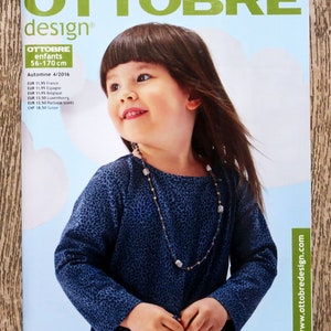 May include: A magazine cover featuring a young girl wearing a blue and white patterned long-sleeved shirt with a beaded necklace. The magazine is titled "Ottobre design®" and the text "enfants 56-170 cm" is also visible. The magazine cover is for the Autumn 4/2016 issue.
