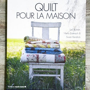 Peut inclure: Un livre intitulé "Quilt Pour La Maison" avec une chaise blanchie à la chaux et une pile de courtepointes colorées dessus. La couverture du livre présente un fond de pelouse verte et le texte "35 Créations Dans Un Esprit Simple Et Naturel".