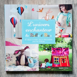 Peut inclure: Couverture de livre illustrant un lapin, des ballons à air chaud et une fille dans une cuisine. Le titre du livre est "L'univers enchanteur de Belle & Boo" et le sous-titre est "25 objets à coudre, jeux et décorations pour les 4-10 ans".