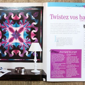 May include: A close-up of a magazine page featuring a colorful quilt pattern with a black background. The quilt is made of fabric strips in shades of pink, blue, and purple. The text on the page reads "Twistez vos bandes (110 cm x 110 cm)" and "Descriptif du projet".
