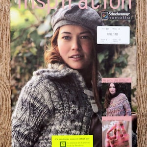 Può includere: Una copertina di rivista con la parola "ispirazione" in grandi lettere rosa. La copertina presenta una donna che indossa un maglione di lana grigio e bianco e un berretto grigio. La rivista si intitola "Schachenmayr nomotta" e ha il testo "RFG. 110" sulla copertina.