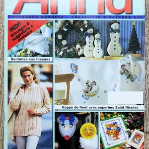 May include: A magazine cover featuring a colorful illustration of three snowmen, a Christmas tree, and a wreath. The magazine is titled "Anna" and is a French publication. The cover also features a variety of craft projects, including a knitted sweater, a crocheted tablecloth, and a children's craft project.