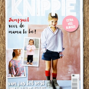 May include: A magazine cover with the title "KNIPPIE" and the text "Jumpsuit voor de mama to be!"  The cover features a young girl wearing a light blue shirt, denim shorts, and red and gray socks. The magazine is titled "KNIPPIE" and the text "EXTRA VEEL BLOUSES" is in a pink circle.