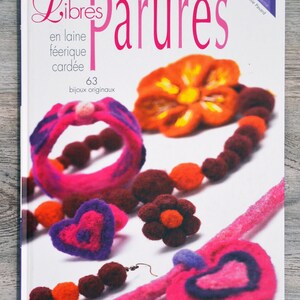 Può includere: Un libro intitolato "Libres Parures" con il sottotitolo "en laine féerique cardée" e il numero "63" sotto. La copertina del libro presenta una varietà di gioielli in feltro colorati, tra cui collane, braccialetti, orecchini e anelli. I gioielli sono realizzati con diversi colori di feltro, tra cui rosa, viola, arancione e marrone.