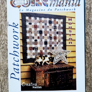 Peut inclure: La couverture du magazine "Quiltmania" présente un patchwork avec un motif en forme d'étoile. Le titre du magazine est en lettres colorées. La couverture comprend également le texte "Le Magazine du Patchwork" et "Houston". Une étoile décorative et une figurine de chat sont sur un coffre.