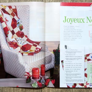 Op de afbeelding: Een rood-witte patchworkdeken met een kerstthema. De deken is over een witte fauteuil met een bloemenpatroon gelegd. De deken is 215 cm x 100 cm.