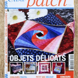 Può includere: Copertina della rivista "Ewa patch" numero 13, con un design astratto colorato e la scritta "Objets Délicats". Presenta immagini di una borsa, un paesaggio, un cuscino e una borsa tote. La rivista è su una superficie di legno.