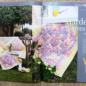 May include: A purple and white floral quilt with a yellow border. The quilt is displayed on a table with a white surface. The text "Garden flowers quilt (100 cm x 160 cm)" is printed on the page.