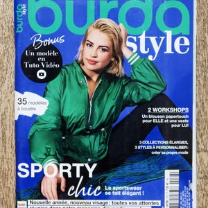 May include: A magazine cover featuring a woman wearing a green jacket. The magazine is titled "burda style" and has the words "Sporty chic" in large letters. The cover also includes the text "2 Workshops", "3 Collections Enlarged", and "3 Styles to Personalize".