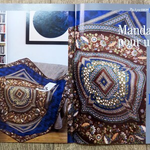 May include: A large, colorful mandala quilt with a brown, blue, and gold color scheme. The quilt is made up of many intricate geometric shapes and patterns. The quilt is called "Mandala pour un roi" and is 120 cm by 120 cm.