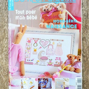 以下が含まれることがあります： 「Bébé dort」と「Naissance」の文字が書かれた、ピンクと白のクロスステッチのデザインが施された雑誌の表紙。表紙には、ピンクと白のぬいぐるみうさぎ、テディベア2体、ピンクと白のギンガムチェックの背景も描かれている。