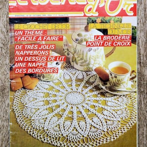 Könnte beinhalten: Ein Vintage-Magazin-Cover mit dem Titel "Crochet d'Or" mit einer weißen gehäkelten Tischdecke, einer Blumenvase und einer Teetasse mit Tee. Das Cover enthält französischen Text mit dem Thema "Einfach zu machen" und "Kreuzstich".