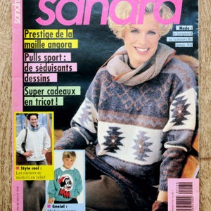 Op de afbeelding: Een tijdschriftomslag met de titel "Sandra" in roze. De cover toont een vrouw in een trui met patroon. Tekst bevat "Les Plus Beaux Tricots" en "Super cadeaux en tricot!". Extra afbeeldingen tonen truien en een kind in een Mickey Mouse trui.