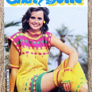 Könnte beinhalten: Eine Frau trägt ein gelbes, pinkfarbenes und grünes Strickkleid mit passendem Strickband und Beinstulpen. Das Kleid hat ein farbenfrohes geometrisches Muster. Das Magazincover lautet "Chat Botte" und "N° 1 RELAX".
