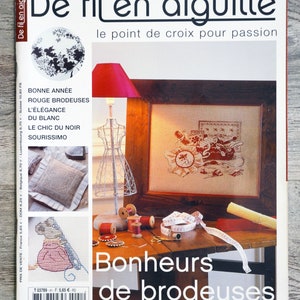 May include: A magazine cover titled "De fil en aiguille" with the subtitle "le point de croix pour passion." The cover features a framed cross-stitch, spools of thread, and the text "Bonheurs de brodeuses."