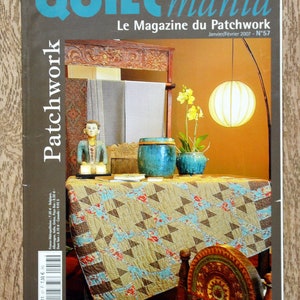 Pode incluir: Uma capa de revista para Quilt Mania, uma revista de patchwork. A capa apresenta um edredom com um padrão geométrico em tons de marrom, azul e branco. O edredom é exibido em uma mesa com uma cadeira de madeira e uma lâmpada no fundo. O título da revista está em texto azul e branco e o texto "Le Magazine du Patchwork" está em texto preto. O número da revista é 57 e a data é janeiro/fevereiro de 2007.