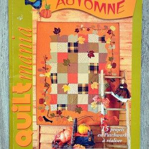 Può includere: Una copertina di rivista con una trapunta patchwork con foglie autunnali e zucche. La rivista si chiama "Quilt Mania" e la copertina riporta "Automne" e "Numéro Spécial". La rivista è di settembre 2004.