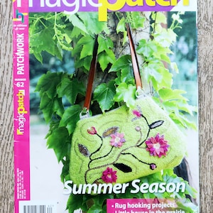 May include: A green crocheted bag with floral embellishments and a brown strap. The bag is hanging from a tree branch. The magazine cover reads "Magic Patch Summer Season" and lists rug hooking projects, a little house in the prairie, and beautiful bears.