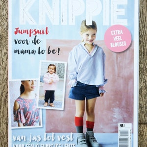 May include: A magazine cover with the title "KNIPPIE" in large, white letters. The cover features a young girl wearing a light blue shirt and denim shorts. The text "Jumpsuit voor de mama to be!" is in black letters on a light blue background. The text "EXTRA VEEL BLOUSES" is in white letters on a pink circle. The text "van jas tot vest VOOR EEN KLEURRIJKE LENTE" is in black letters on a light blue background.