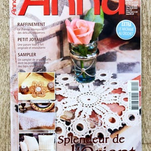 May include: A magazine cover featuring the title "Anna" in large red letters. A pink rose in a small glass vase sits atop a white crocheted doily. The cover also includes the text "Splendeur de l'Orient".