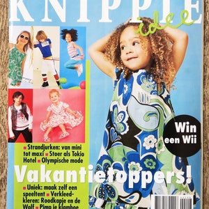 May include: A magazine cover with the title "KNIPPIE" and the text "Vakantietoppers!"  The cover features a young girl wearing a blue and green floral dress. The magazine is advertising a contest to win a Wii.