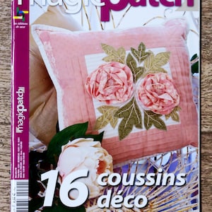 Pode incluir: Uma capa de revista com um travesseiro rosa com um design floral. A revista é intitulada "magicpatch" e o texto "16 coussins déco" é visível. A capa da revista também inclui o texto "Appliqué Stitcheries Pliage Crochet".