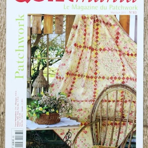 Op de afbeelding: De cover van het tijdschrift "Quiltmania" toont een patchwork-ontwerp. De titel is rood, met "Le Magazine du Patchwork" eronder. De cover bevat een bloemenquilt, een rieten stoel en een bloemenmand, wat een rustieke scène creëert.