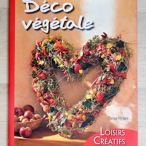 Puede incluir: Un libro titulado "Déco végétale" con una cubierta roja y una corona en forma de corazón hecha de flores secas, hojas y chiles. El libro forma parte de la serie "Loisirs Créatifs" y es publicado por "les éditions de saxé".