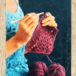 Può includere: Immagine di una copertina di libro all'uncinetto con il titolo "La petite encyclopédie du crochet". L'immagine mostra mani che lavorano all'uncinetto un pezzo di tessuto bordeaux, con due gomitoli di lana bordeaux in basso. A sinistra è visibile un top all'uncinetto blu.