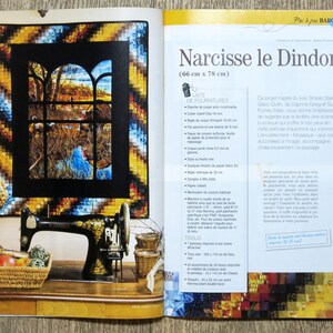 Op de afbeelding: Een kleurrijk naaldwerkproject met de titel "Narcisse le Dindon" (66 cm x 78 cm) met instructies voor het maken van het project. Het project toont een raam met een vogel en een blauwe lucht.