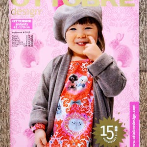 May include: A magazine cover with a child in a grey beret and cardigan, and a patterned dress. The magazine is "OTTOBRE design" with the text "enfants 62-170 cm". The cover has a pink background with pink bunny illustrations and text in French.