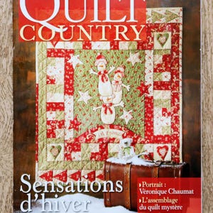 Op de afbeelding: De cover van het tijdschrift "Quilt Country" toont een winterthema quilt met sneeuwmannen, sterren en harten in rood, groen en wit. De titel van het tijdschrift staat in grote rode letters, met de woorden "Sensations d'hiver" eronder.
