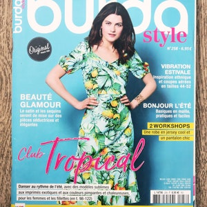 May include: A magazine cover featuring a woman in a tropical print dress. The magazine is titled "Burda Style" and has the words "Club Tropical" in large pink letters. The cover has a turquoise background and text in French.