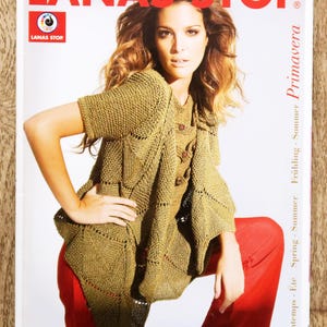 May include: A magazine cover featuring a woman wearing a knitted olive green top and red pants. The magazine title "LANAS STOP" is in large red letters. The cover also includes text in multiple languages, including "Spring - Summer - Primavera".