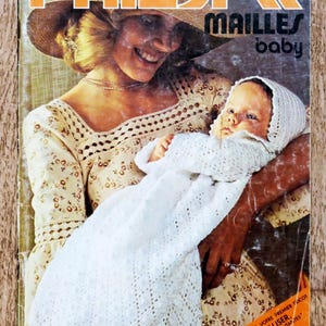 Könnte beinhalten: Vintage Zeitschriften-Cover mit dem Titel "PHILDAR MAILLES baby" in Orange. Das Bild zeigt eine Frau, die ein Baby hält, das in eine weiße gehäkelte Decke gewickelt ist. Das Cover hat eine Retro-Ästhetik.