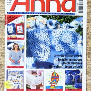 May include: A magazine cover for Anna, a French publication for crafting and home decor. The cover features a variety of projects, including crocheted doilies, embroidered tablecloths, and fabric bags. The text on the cover reads "Ouvrages Manuels - Créativité d'aujourd'hui" which translates to "Manual Work - Creativity of Today".