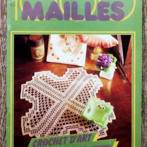 Könnte beinhalten: Ein Vintage-Magazin-Cover mit dem Titel "100 MAILLES" in lila Buchstaben auf grünem Hintergrund. Das Cover zeigt eine gehäkelte Tischdecke, eine kleine grüne Schale und andere dekorative Gegenstände.