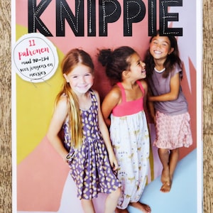 May include: A magazine cover with the title "KNIPPIE" in black text with white stitching. The cover features three girls wearing colorful dresses and the text "11 patronen maal 98-134 voor jongens en meisjes".
