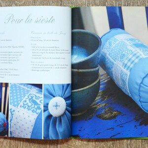 May include: A book open to a page with instructions for making a blue and white pillow. The page includes a list of materials and measurements in centimetres. The image also shows a blue and white pillow on a blue chair.