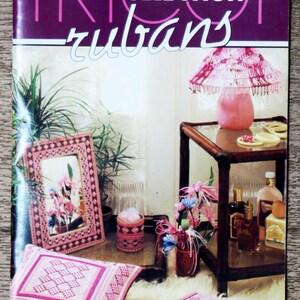 May include: A magazine cover with the title "TRICOT SELECTION rubans" in purple and white. The image features a pink lamp, a framed picture, a pillow, and other decorative items, all in shades of pink and white. The scene suggests a focus on home decor and crafts.