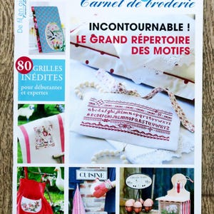 Könnte beinhalten: Ein Magazin-Cover für eine französische Stickerei-Publikation namens "De Fil en Aiguille" mit dem Text "Incontournable! Le Grand Repertoire Des Motifs" und einem Foto eines weißen Kissens mit roten Nähten und einem weißen Handtuch mit roten Nähten. Das Magazin-Cover zeigt auch ein Foto eines weißen Handtuchs mit roten Nähten und dem Text "80 Grilles Inédites pour débutantes et expertes".