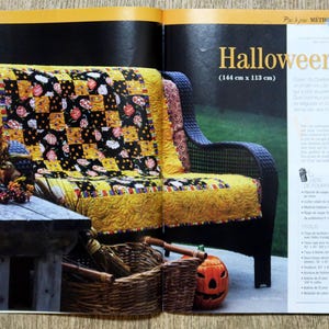 Op de afbeelding: Een zwarte rieten bank met een gele, zwarte en oranje Halloween-thema deken. De bank is 144 cm breed en 113 cm diep. De bank staat op een houten vloer met een kleine houten tafel ervoor.