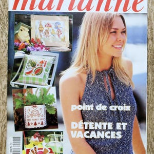 Può includere: Una copertina di rivista con il titolo "les idées de marianne" in rosso. La copertina presenta progetti di punto croce, una donna con un top blu e il testo "point de croix DETENTE ET VACANCES".