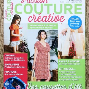 Op de afbeelding: De cover van het tijdschrift "Passion Couture Créative" toont een vrouw in een rode jurk en een meisje in een oranje top. Het adverteert naaipatronen en projecten, gedateerd juli-september 2021.