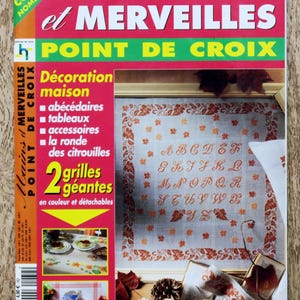 Könnte beinhalten: Titelseite der Zeitschrift "Mains et Merveilles" mit dem Titel "Point de Croix". Das Cover zeigt Kreuzstichmuster, darunter ein Alphabet und dekorative Bordüren, in Rot- und Orangetönen.