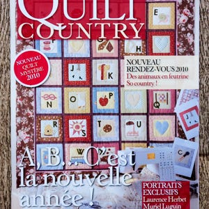 Puede incluir: Portada de la revista "QUILT COUNTRY" con un diseño rojo y blanco. Presenta una cuadrícula de coloridos cuadrados de edredón con letras e imágenes. El texto incluye "NOUVEAU QUILT MYSTÈRE 2010" y "A, B... C'est la nouvelle année!"