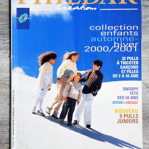 May include: A magazine cover featuring a group of children in a sandy landscape. The magazine is titled "PHILDAR Creations" and features the text "collection enfants automne-hiver 2000/2001". The cover also includes the text "32 Pulls à tricoter garçons et filles de 2 à 16 ans", "Snoopy fête ses 50 ans", "Peanuts 50th Celebration", and "Nouveau 9 Pulls Juniors".