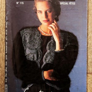 Peut inclure: Couverture du magazine "ann blatt" avec une femme en tenue noire ornée de motifs perlés. La couverture affiche "SPÉCIAL FÊTES" et "Créez votre séduction". Le magazine est posé sur une surface en bois.